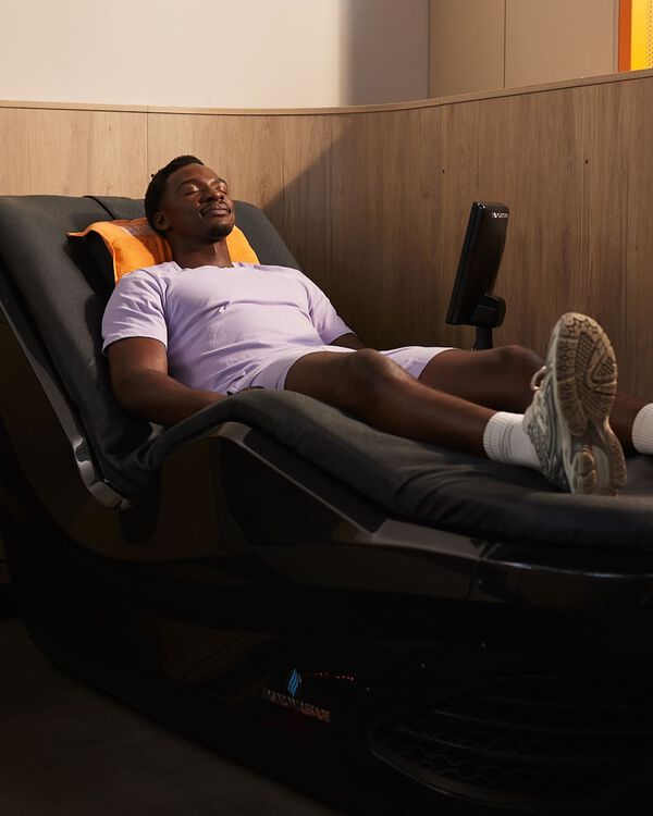 Een man in een lichtpaarse sportoutfit ontspant op een hydromassagebed met een oranje handdoek achter zijn hoofd bij Basic-Fit.